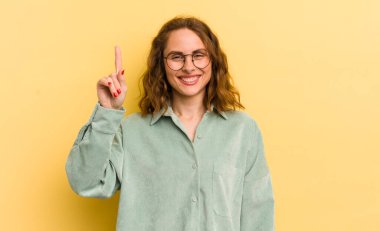 Genç ve güzel bir kadın mutlu bir şekilde gülümsüyor, tek eliyle yukarıyı göstererek boşluğu kopyalıyor.