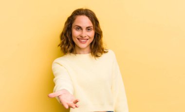 Genç, güzel bir kadın gülümsüyor, mutlu, kendinden emin ve arkadaş canlısı görünüyor, bir anlaşmaya varmak için el sıkışmayı teklif ediyor, işbirliği yapıyor.