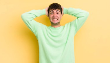 Genç ve yakışıklı bir adam stresli, endişeli, endişeli ya da korkmuş, elleri başının üstünde, hata yaptığında panikliyor.