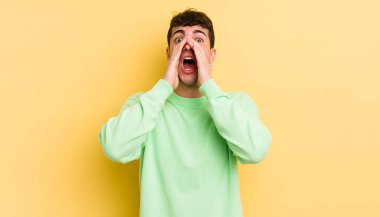 Genç yakışıklı adam mutlu, heyecanlı ve pozitif hissediyor. Elleri ağızda, bağırıyor.