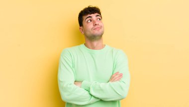 Genç yakışıklı adam omuz silkiyor, kafası karışık ve kararsız, kolları bağlı ve şaşkın görünüyor.