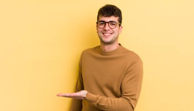 Genç yakışıklı adam neşeyle gülümsüyor, mutlu hissediyor ve fotokopi uzayında bir konsept gösteriyor.