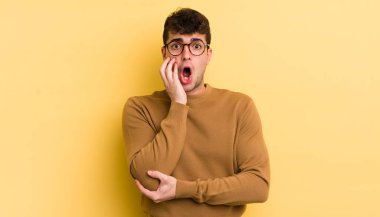 Genç yakışıklı adam şok ve inançsızlık içinde, elleri yanak ve kolları çapraz, sersemlemiş ve şaşırmış hissediyor.