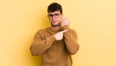 Genç yakışıklı adam sabırsız ve kızgın görünüyor, saati gösteriyor, dakiklik istiyor, zamanında gelmek istiyor.
