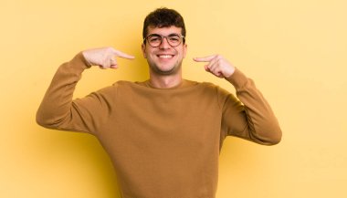 Genç yakışıklı adam, kendine güvenerek gülümsüyor. Geniş bir gülümseme, pozitif, rahat, tatmin olmuş bir tavır.