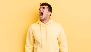 Genç yakışıklı adam öfkeyle bağırıyor, agresif bir şekilde bağırıyor, stresli ve sinirli görünüyor.