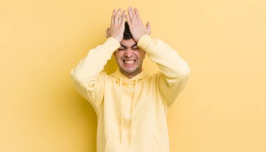 Genç ve yakışıklı bir adam stresli ve endişeli, depresyonda ve hayal kırıklığına uğramış, iki elini de başa kaldırıyor.