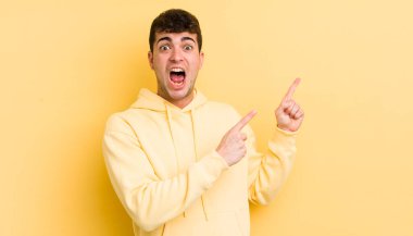 Genç, yakışıklı bir adam kendini neşeli ve şaşırmış hissediyor. Şok olmuş bir ifadeyle gülümsüyor ve bir tarafı işaret ediyor.