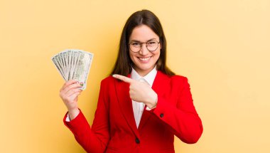 Genç, güzel bir kadın neşeyle gülümsüyor, mutlu hissediyor ve bir tarafı işaret ediyor. para kavramı