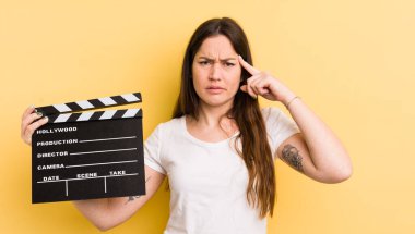 Genç ve güzel bir kadın kafası karışık ve şaşkın hissediyor, deli olduğunu gösteriyor. Sinema alkışlama konsepti