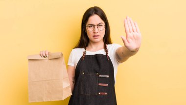 Genç ve güzel bir kadın ciddi görünüyor. Avuç içini gösteriyor. Durdurma hareketi yapıyor. Fast food kuryesi