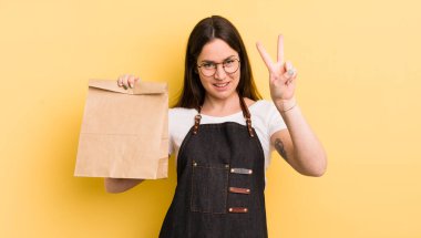 Genç, güzel bir bayan gülümsüyor ve iki numarayı gösteriyor. Fast food kuryesi