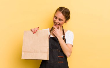 Genç ve güzel bir kadın, mutlu ve kendinden emin bir ifadeyle gülümsüyor, elleri çenesinde. Fast food kurye konsepti