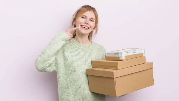 redhead pretty girl smiling confidently pointing to own broad smile. shipping boxes concept