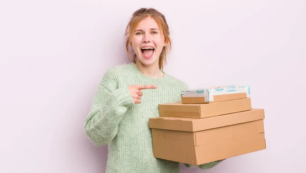 赤頭の可愛い女の子が興奮して驚いて横を指差した 配送ボックスのコンセプト — ストック写真