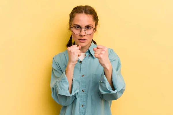 young pretty woman looking confident, angry, strong and aggressive, with fists ready to fight in boxing position