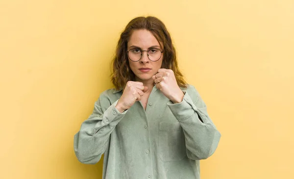 young pretty woman looking confident, angry, strong and aggressive, with fists ready to fight in boxing position