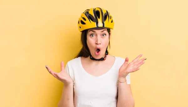 young pretty woman amazed, shocked and astonished with an unbelievable surprise. bike helmet concept