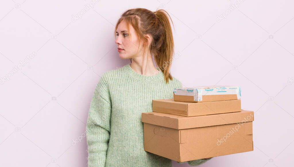 redhead pretty girl on profile view thinking, imagining or daydreaming. shipping boxes concept