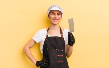 Genç ve güzel bir kadın mutlu bir şekilde gülümsüyor, eli kalçasında ve kendinden emin. Kasap konsepti