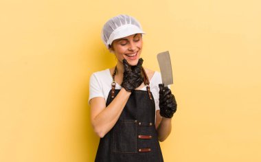 Genç ve güzel bir kadın, mutlu ve kendinden emin bir ifadeyle gülümsüyor, elleri çenesinde. Kasap konsepti