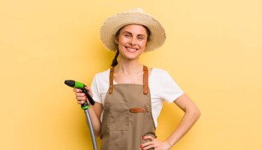 Genç ve güzel bir kadın mutlu bir şekilde gülümsüyor, eli kalçasında ve kendinden emin. gardering konsepti