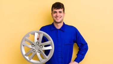 Genç yakışıklı adam mutlu bir şekilde gülümsüyor, eli kalçasında ve kendinden emin. araba tamircisi konsepti