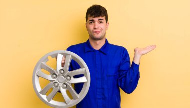 Genç yakışıklı adam şaşkın, şaşkın ve şüpheci hissediyor. araba tamircisi konsepti