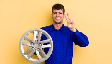 Genç yakışıklı adam gülümsüyor ve mutlu görünüyor, zafer ya da barış işareti yapıyor. araba tamircisi konsepti