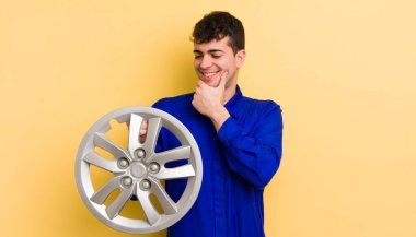 Genç ve yakışıklı bir adam mutlu ve kendinden emin bir ifadeyle gülümsüyor, elleri çenesinde. araba tamircisi konsepti