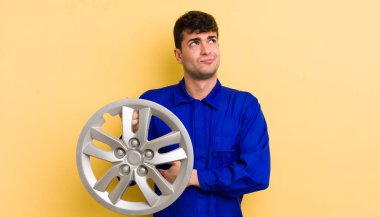 Genç yakışıklı adam omuz silkiyor, kafası karışık ve kararsız. araba tamircisi konsepti