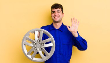 Genç yakışıklı adam mutlu bir şekilde gülümsüyor, el sallıyor, sizi selamlıyor ve selamlıyor. araba tamircisi konsepti