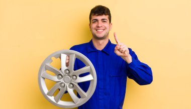 Genç yakışıklı adam gülümsüyor ve arkadaş canlısı görünüyor, bir numarayı gösteriyor. araba tamircisi konsepti