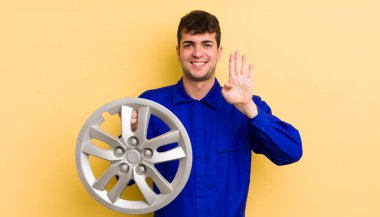 Genç yakışıklı adam gülümsüyor ve arkadaş canlısı görünüyor, dört numarayı gösteriyor. araba tamircisi konsepti