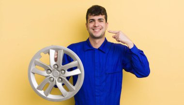 Genç ve yakışıklı bir adam kendi gülüşünü işaret ederek kendine güvenerek gülümsüyor. araba tamircisi konsepti