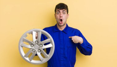 Şok olmuş ve ağzı açık, kendini işaret eden genç ve yakışıklı bir adam. araba tamircisi konsepti