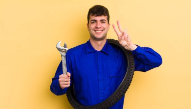 Genç yakışıklı adam gülümsüyor ve arkadaş canlısı görünüyor, iki numarayı gösteriyor. motor tamircisi kavramı