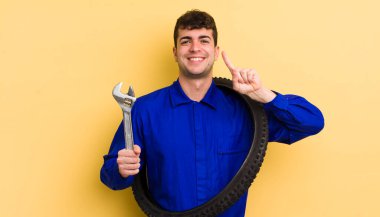 Genç yakışıklı adam gülümsüyor ve arkadaş canlısı görünüyor, bir numarayı gösteriyor. motor tamircisi kavramı