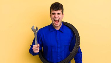 Genç yakışıklı adam agresif bir şekilde bağırıyor, çok kızgın görünüyor. motor tamircisi kavramı