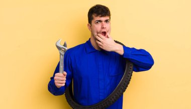 Ağzı ve gözleri açık ve eli çenesinde genç yakışıklı bir adam. motor tamircisi kavramı