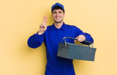 Genç yakışıklı adam gülümsüyor ve arkadaş canlısı görünüyor, iki numarayı gösteriyor. tesisatçı kavramı