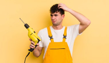 Kafası karışmış, kafası karışmış, kaşınan genç, yakışıklı bir adam. Tamirci ve matkap konsepti