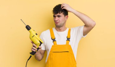 Genç yakışıklı adam mutlu bir şekilde gülümsüyor ve hayal kuruyor ya da şüphe ediyor. Tamirci ve matkap konsepti