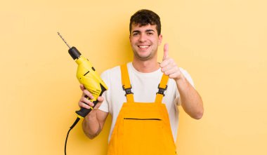 Genç ve yakışıklı bir adam gururlu, olumlu gülümsüyor. Tamirci ve matkap konsepti