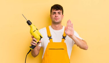 Genç ve yakışıklı adam ciddi görünüyor. Avuç içi gösteriyor. Durdurma hareketi yapıyor. Tamirci ve matkap konsepti