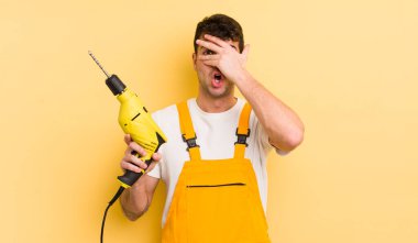 Genç, yakışıklı adam şok olmuş, korkmuş ya da korkmuş görünüyor. Tamirci ve matkap konsepti