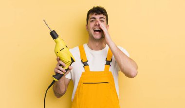 Genç yakışıklı adam mutlu hissediyor, elleri ağzının kenarında bağırıyor. Tamirci ve matkap konsepti