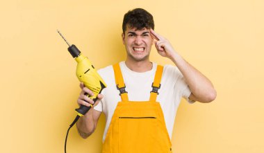 Genç yakışıklı adam kafası karışık ve şaşkın hissediyor, deli olduğunu gösteriyor. Tamirci ve matkap konsepti