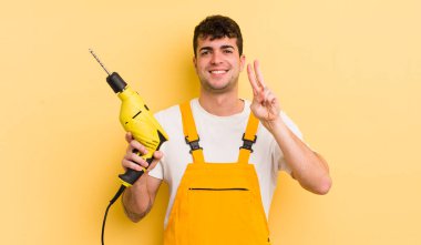 Genç yakışıklı adam gülümsüyor ve arkadaş canlısı görünüyor, iki numarayı gösteriyor. Tamirci ve matkap konsepti