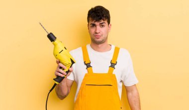 Genç ve yakışıklı bir adam üzgün, üzgün ya da kızgın hissediyor ve yan tarafa bakıyor. Tamirci ve matkap konsepti